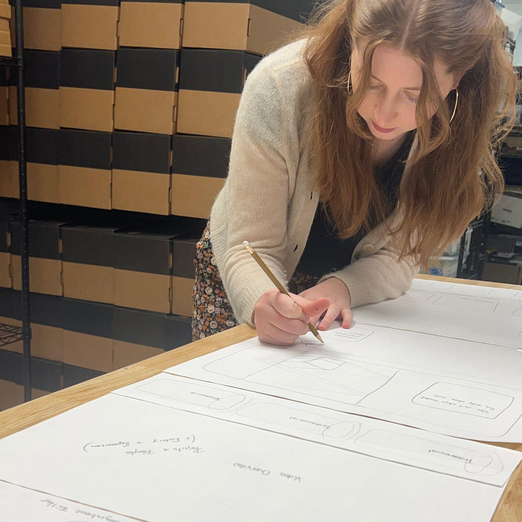 Sophie sketching homepage wireframes on large paper at the packing bench