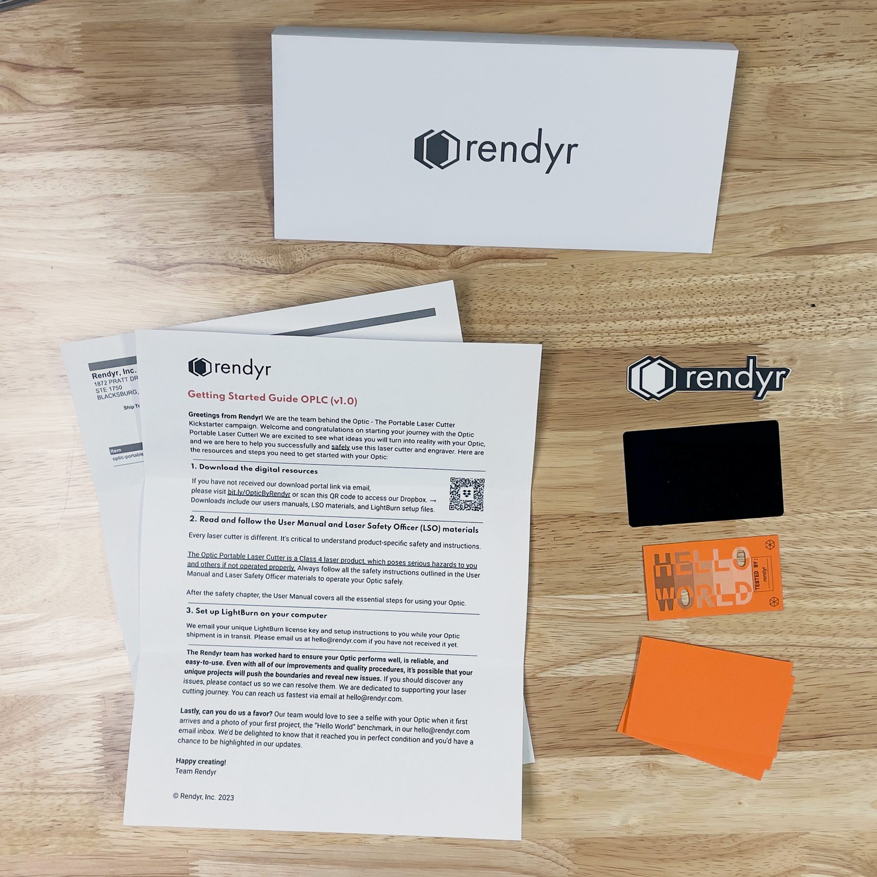 Welcome envelope contents laid out on a workbench: branded envelope, getting started guide, order confirmation slip, logo sticker, protective aluminum card, completed Hello World benchmark, and blank Hello World project cards
